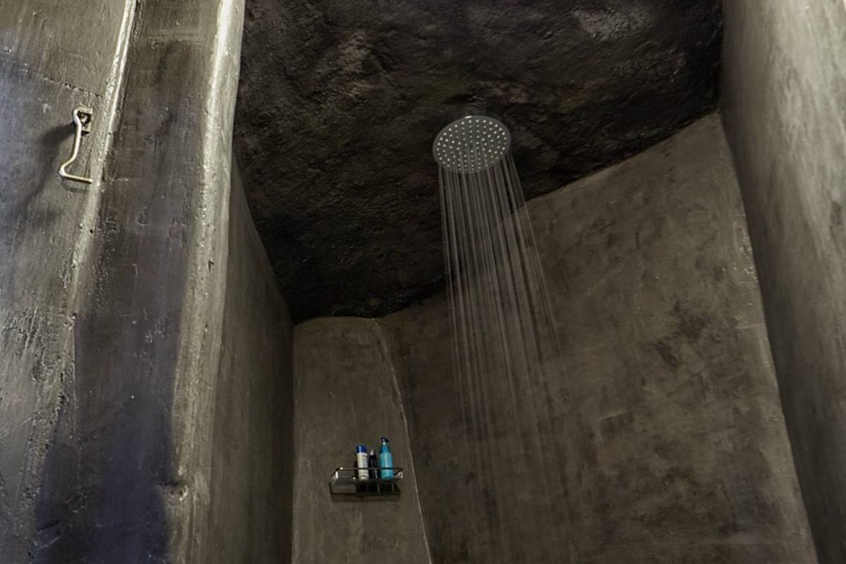 A rain shower under a round skylight in a bathroom carved from volcanic rock