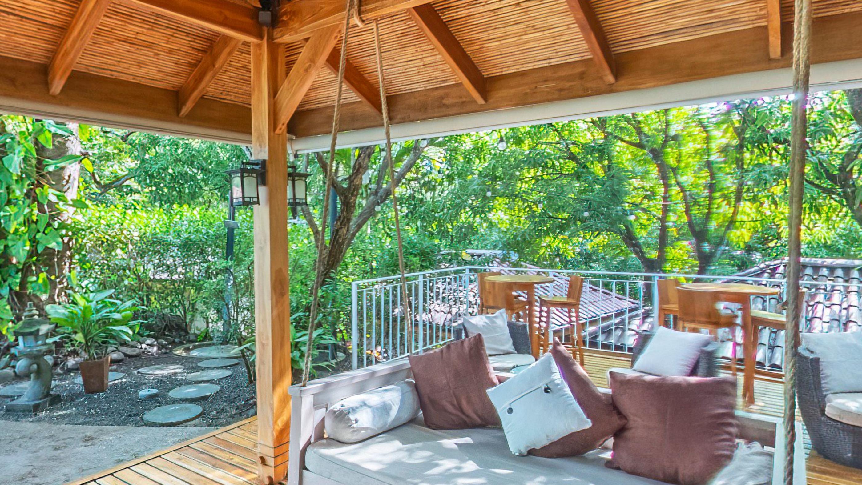Hanging daybeds heaped with cushions on a timber deck, looking out into the trees