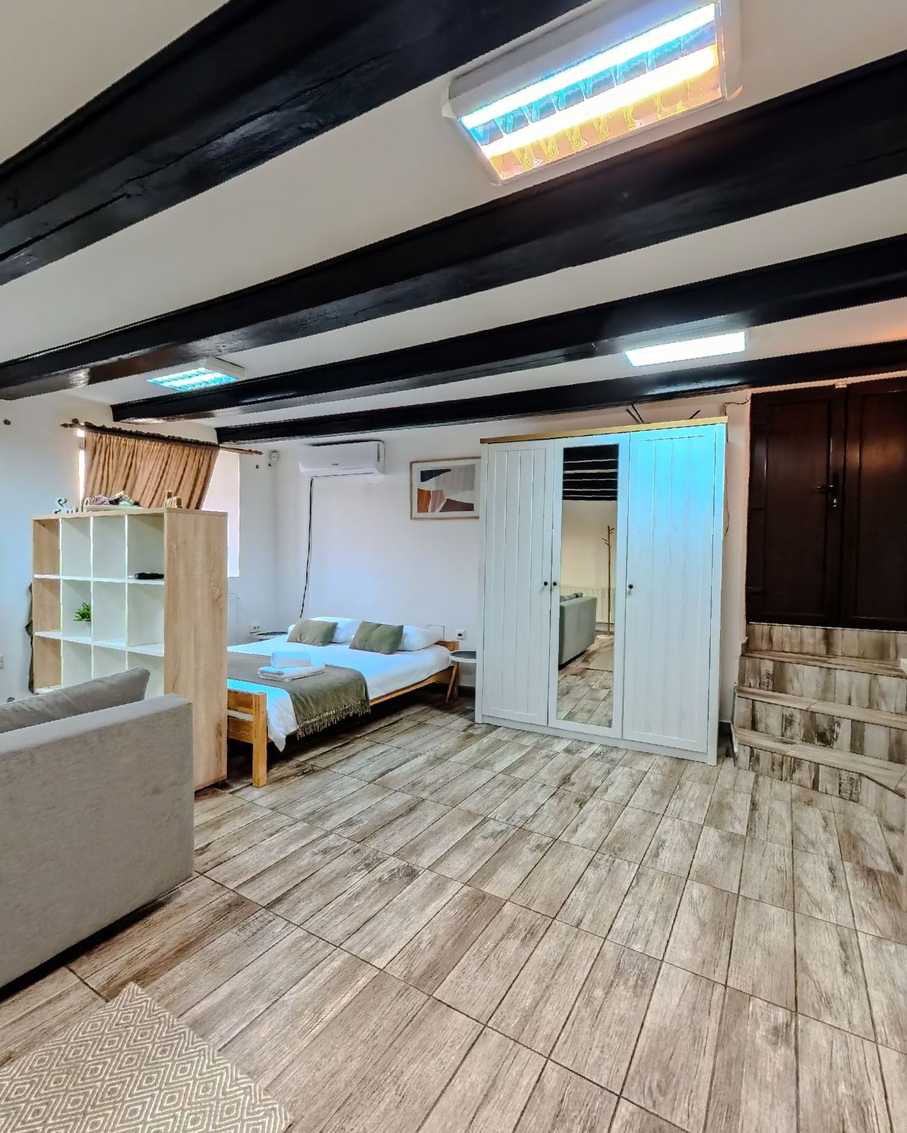 The double bed with white linen and a green throw, under the dark beams