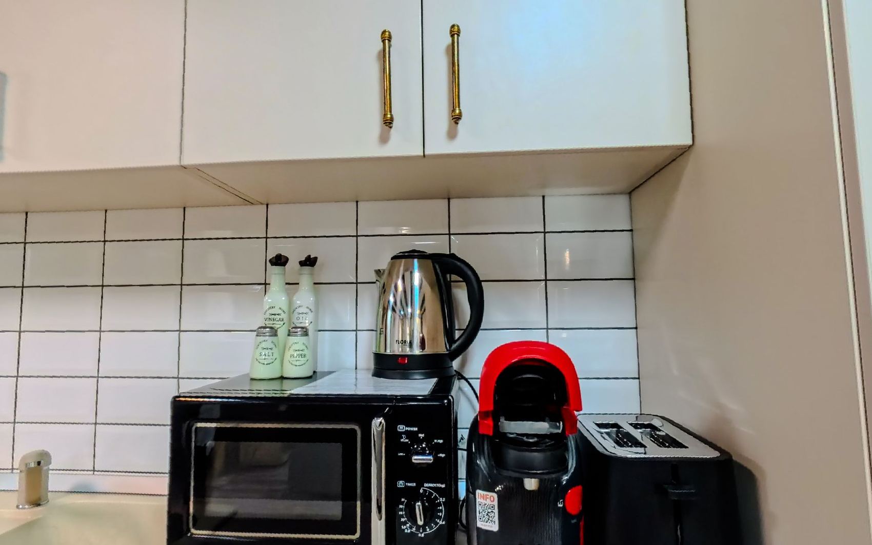 The counter with a microwave, kettle, toaster and coffee machine against white tiles