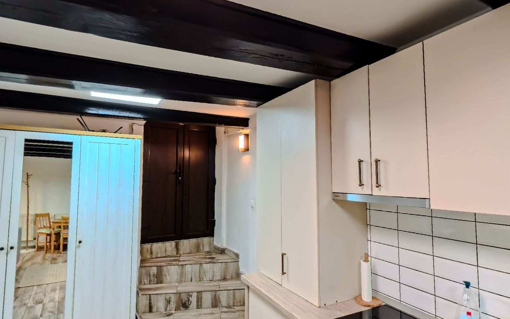 The kitchen end of the room with white cupboards, a tiled splashback and a door through