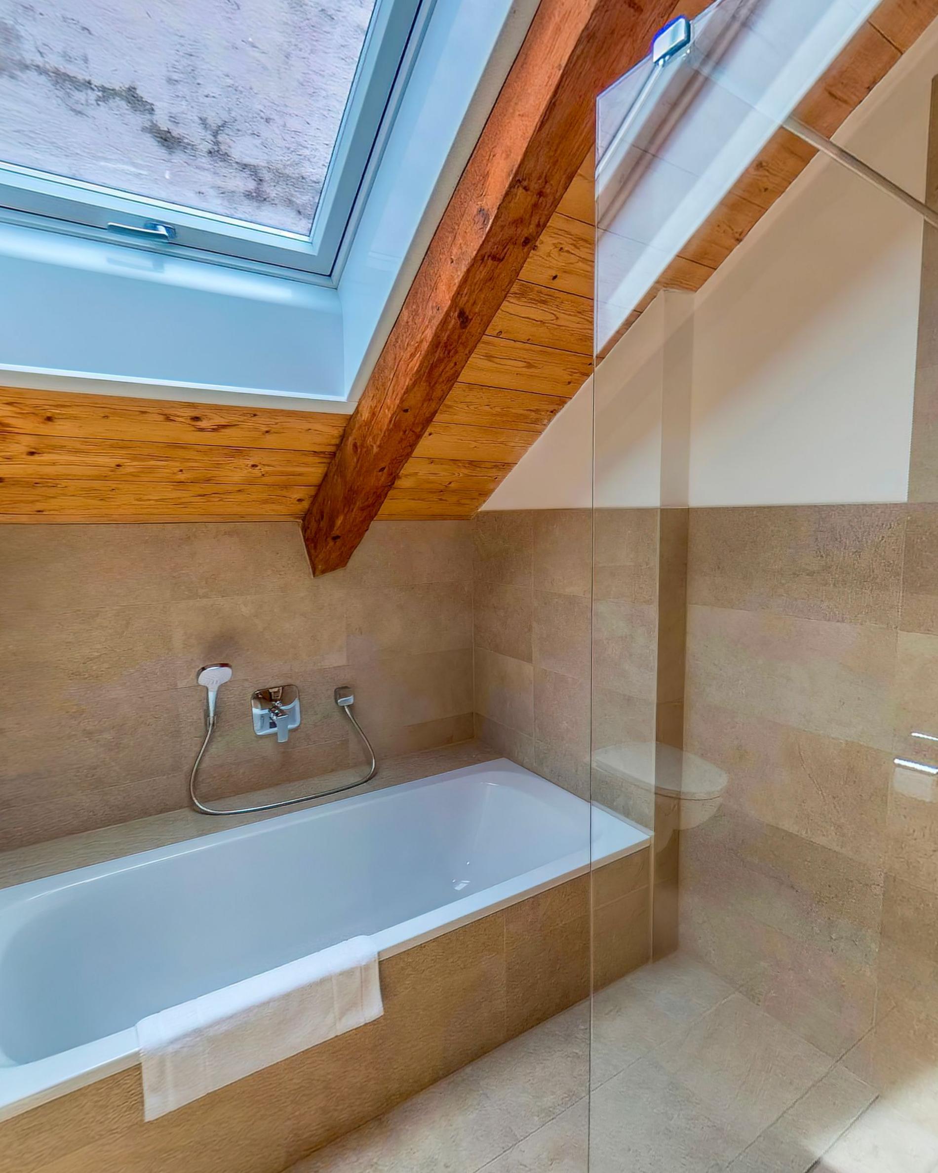 A bath set under the sloping ceiling with a glass screen and daylight from a roof window