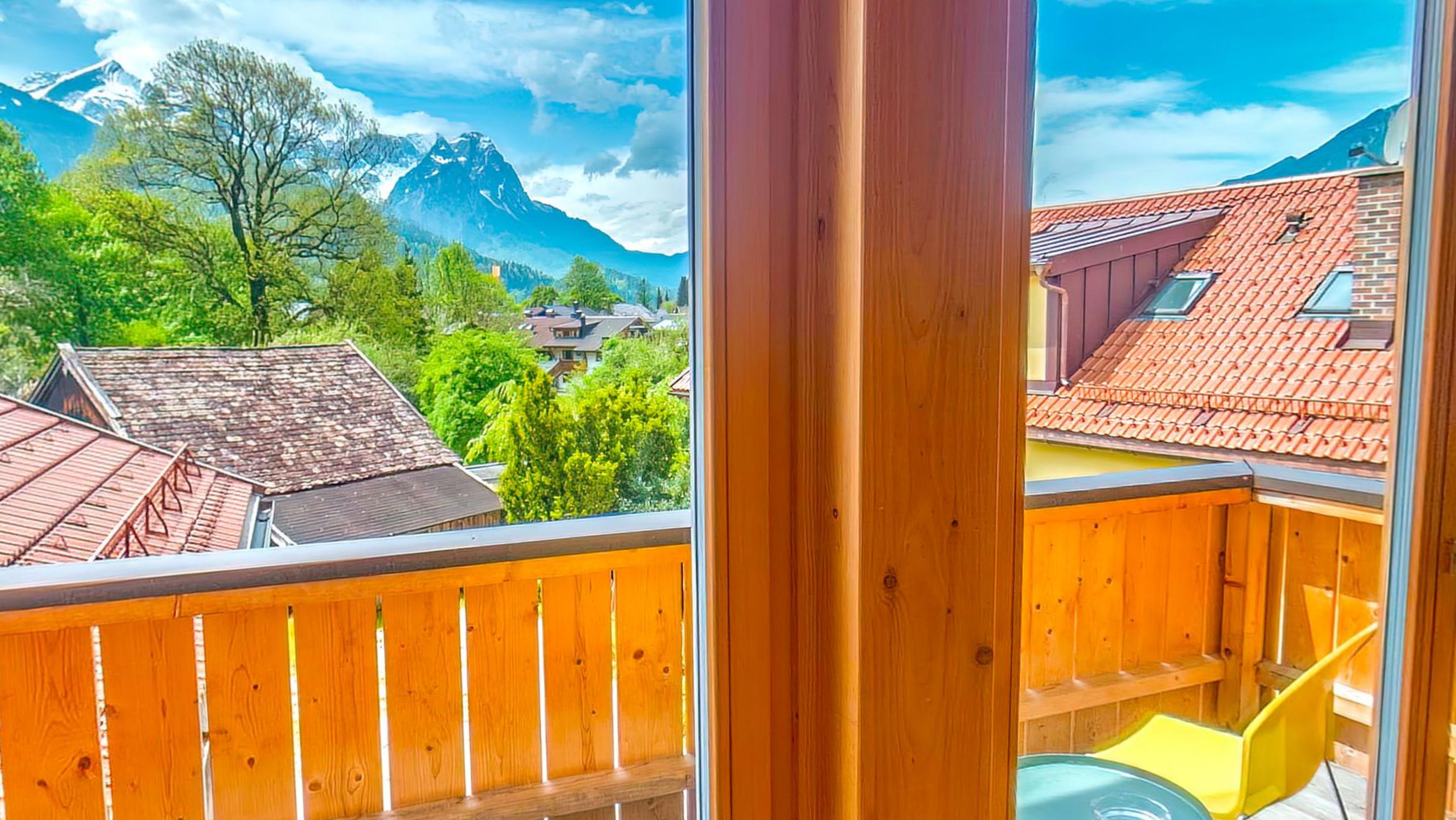 The open balcony door framing a bare tree, red roofs and a snow topped peak