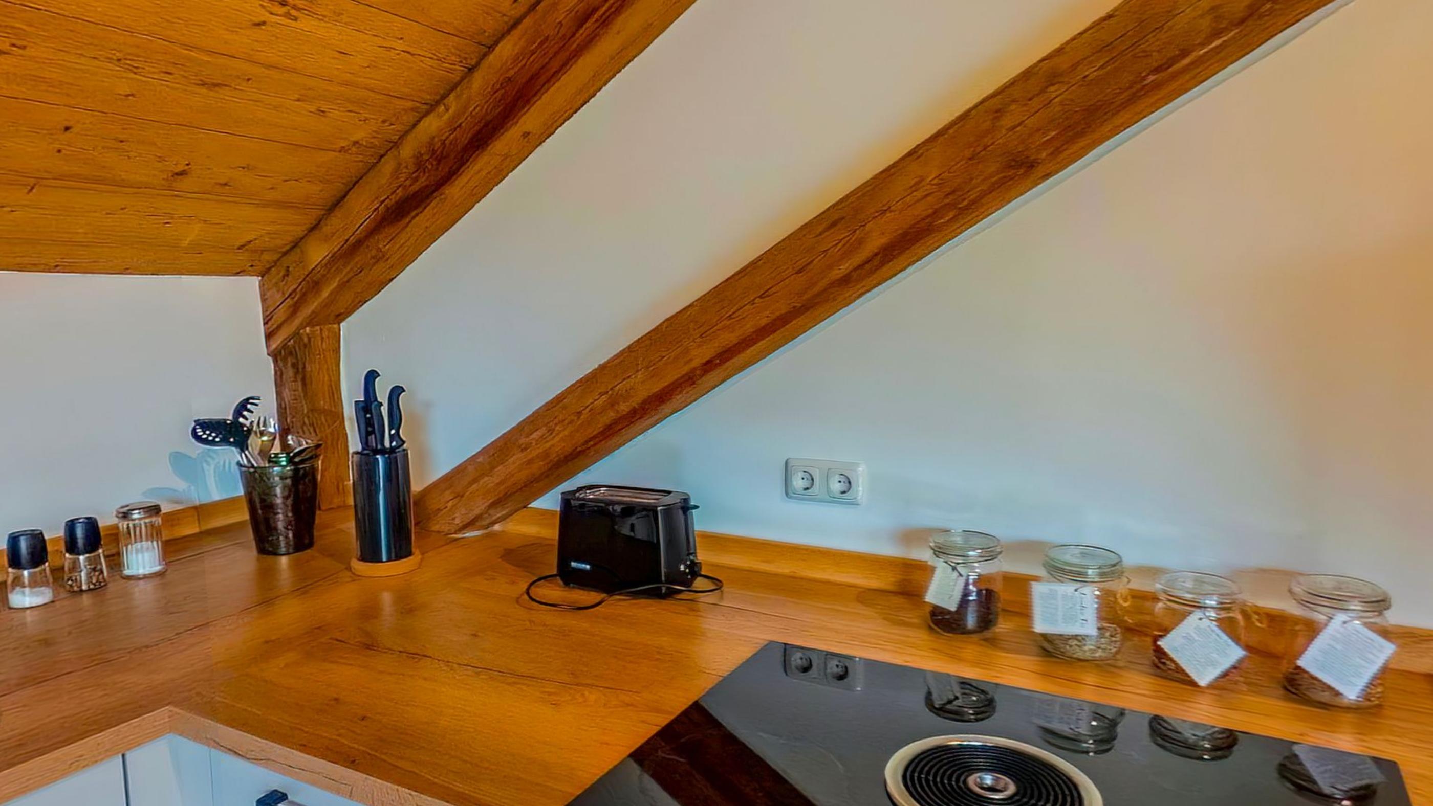 The kitchen worktop with a hob, knife block and glass jars, tucked under the sloping ceiling
