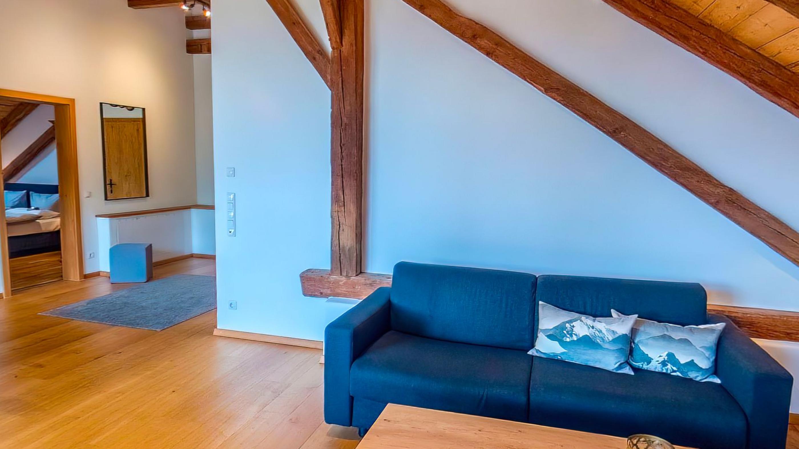 A deep blue sofa with alpine patterned cushions under a heavy timber rafter crossing the white wall