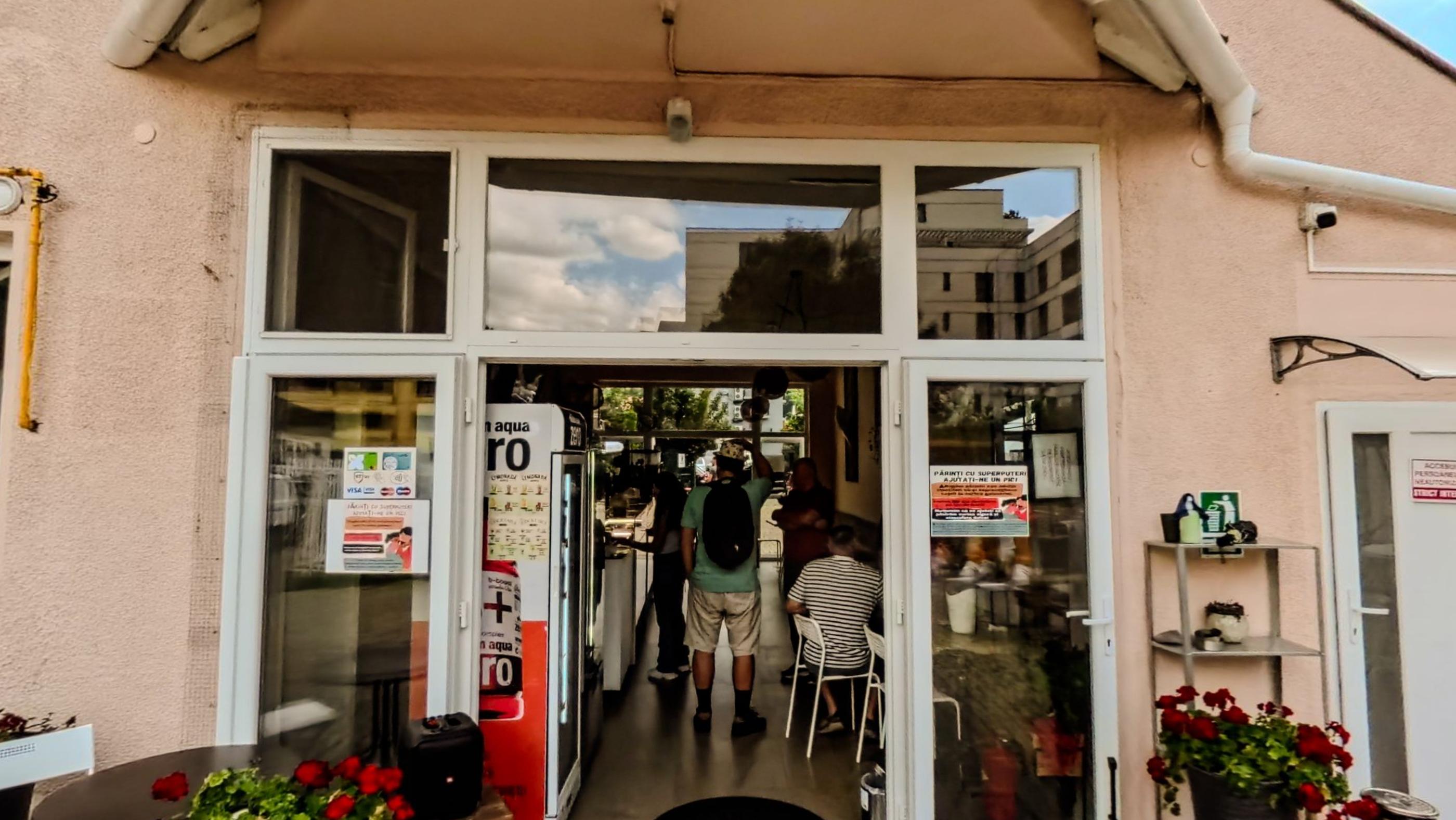 The shop front with glass doors open and geraniums outside