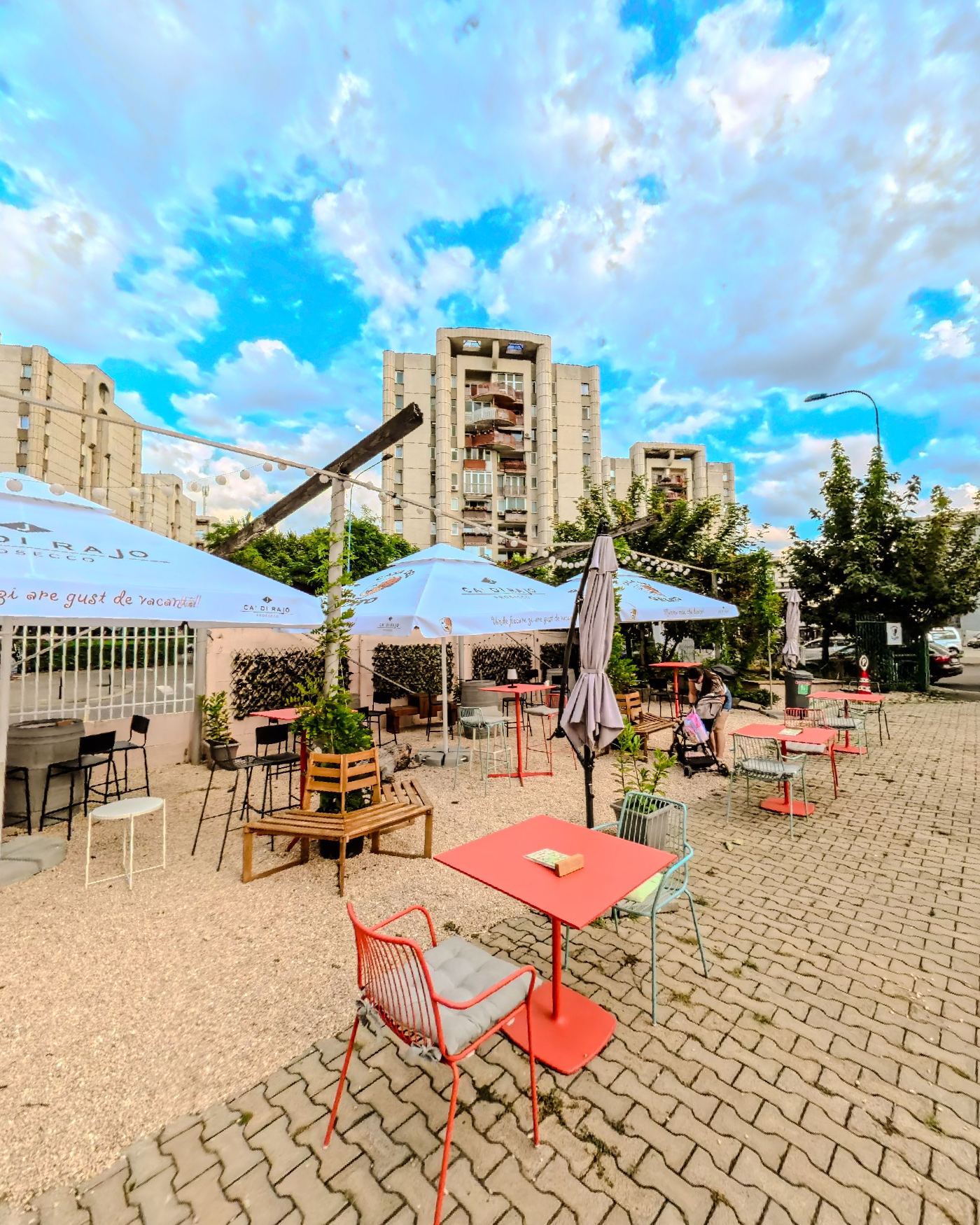 Coral tables and blue parasols on the cobbled terrace under a big sky