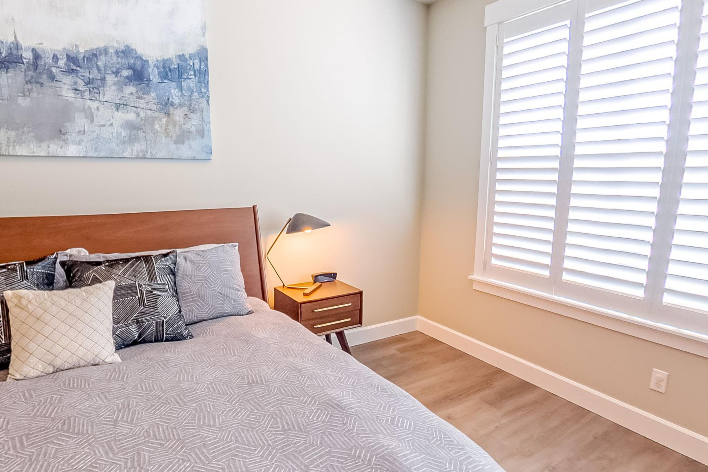 A main bedroom with a made bed, patterned cushions and white window shutters