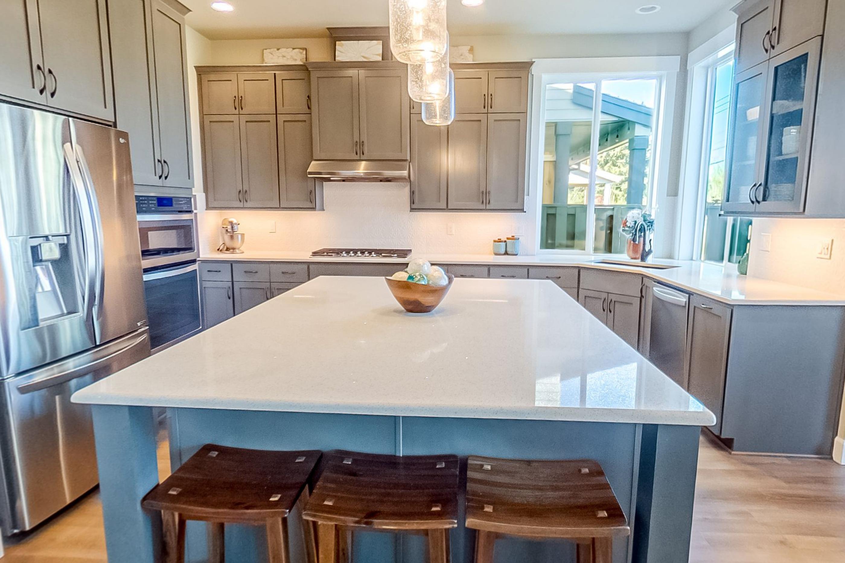 A kitchen island with three timber stools, stainless appliances and grey cabinetry
