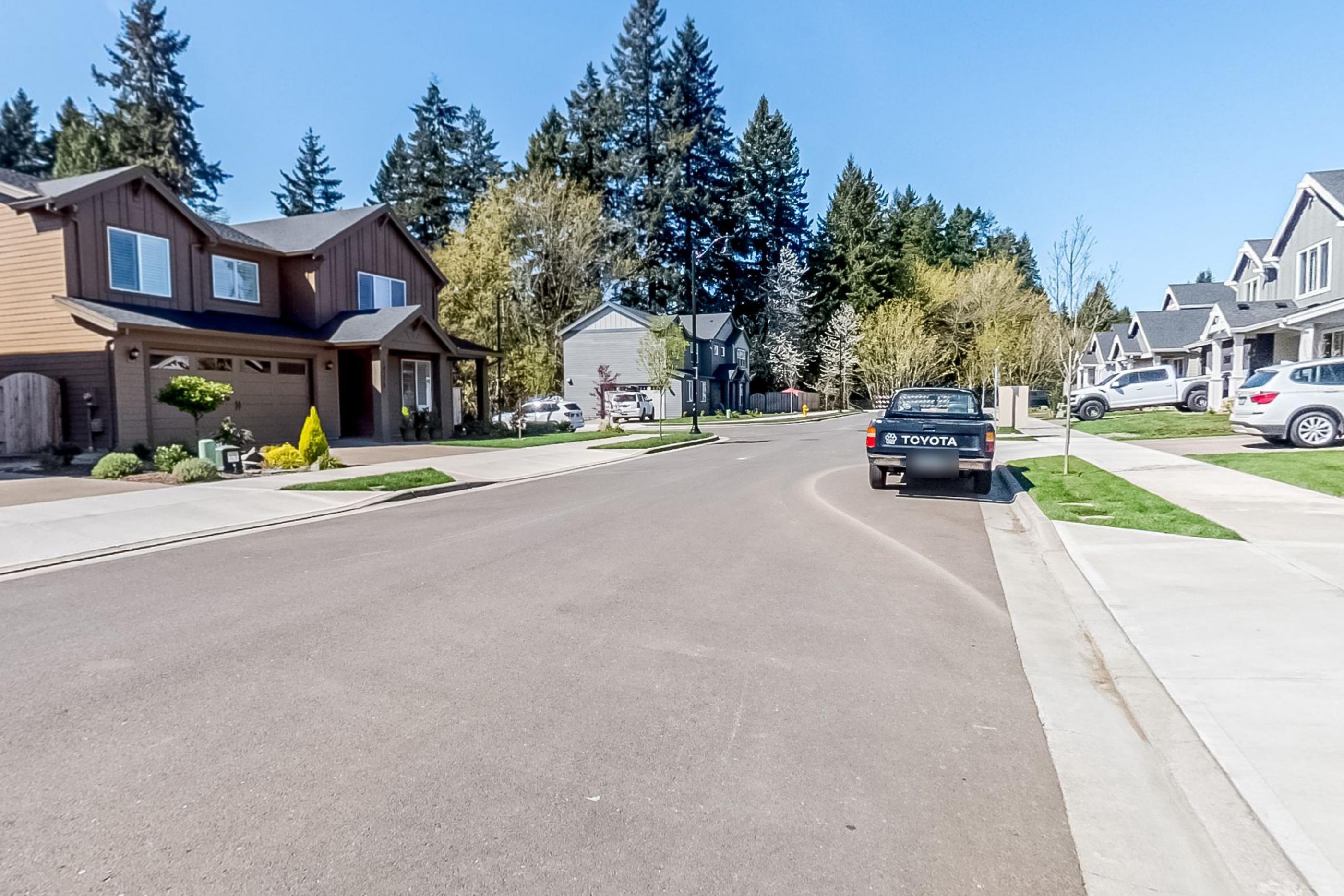 A suburban street of new houses with tall firs behind them and a parked pickup
