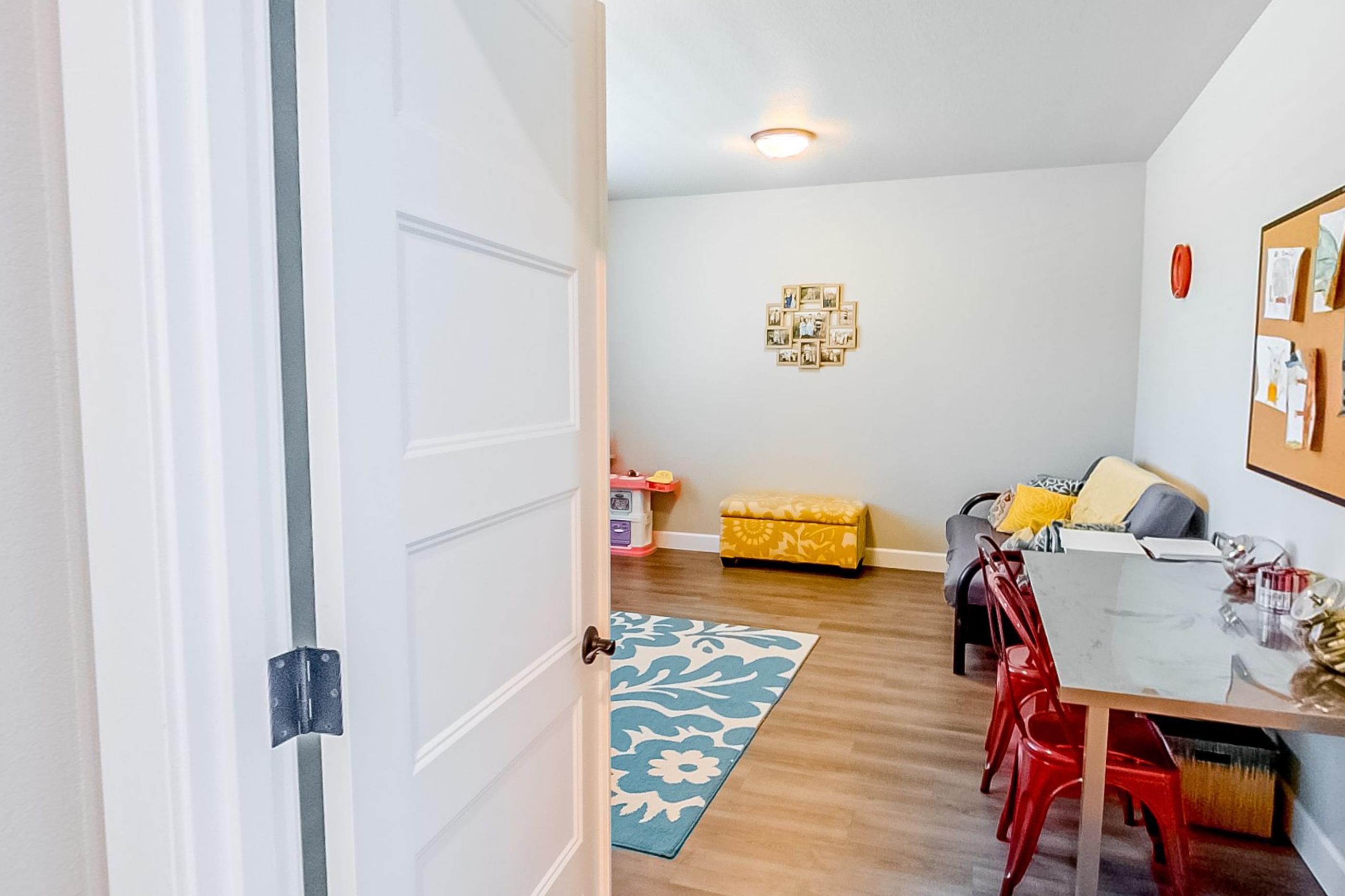A doorway into a children's craft room with a blue rug, a table and red chairs