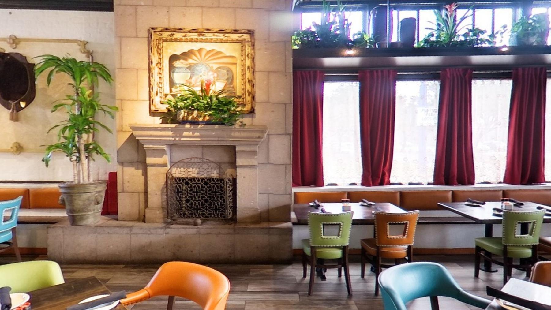 Tables and green chairs around a carved stone fireplace