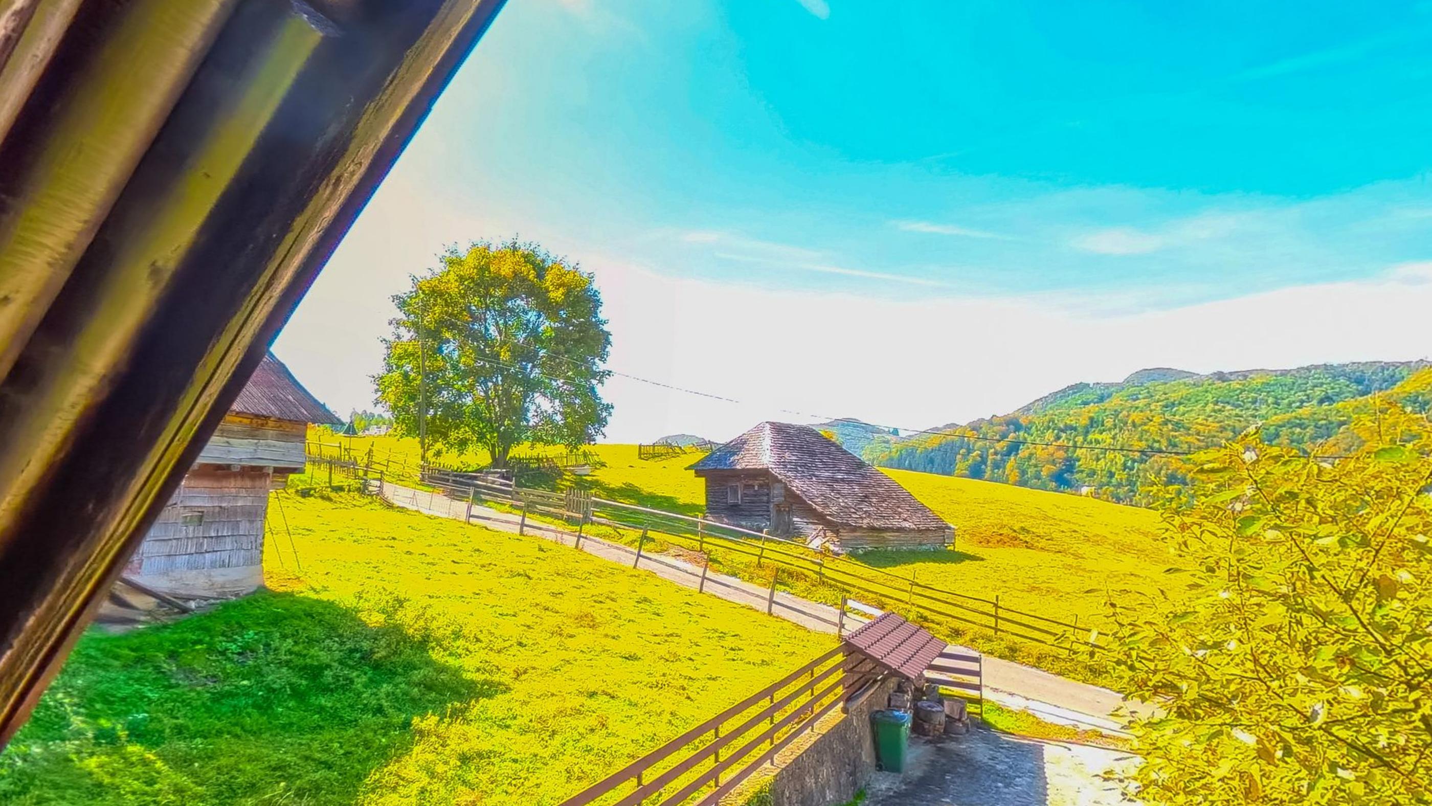 The view from the master bedroom terrace, a timber post in the foreground, a tree, an old stone barn and the hillside beyond