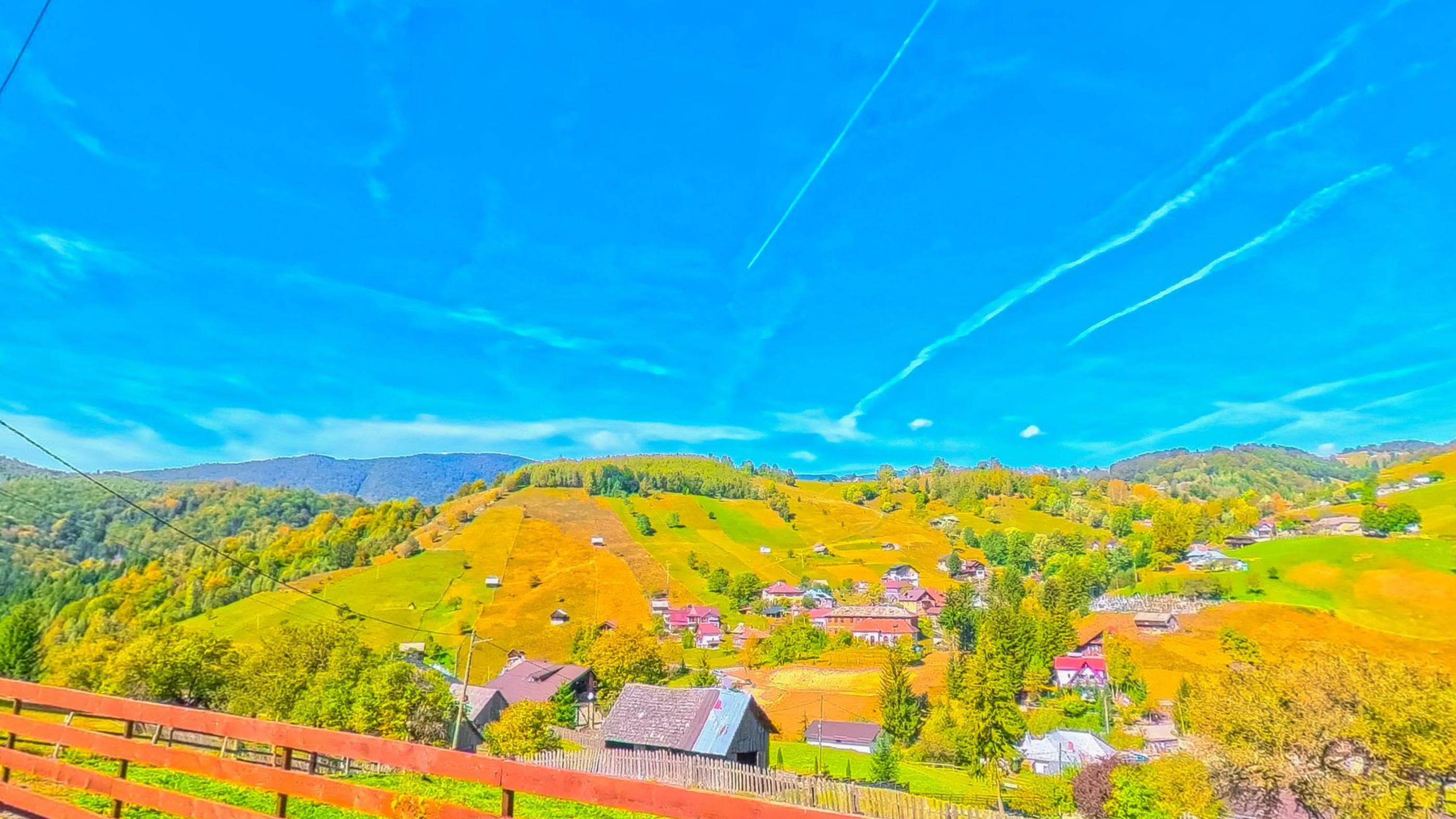 The village below the fence, red roofs among the fields, wooded hills beyond