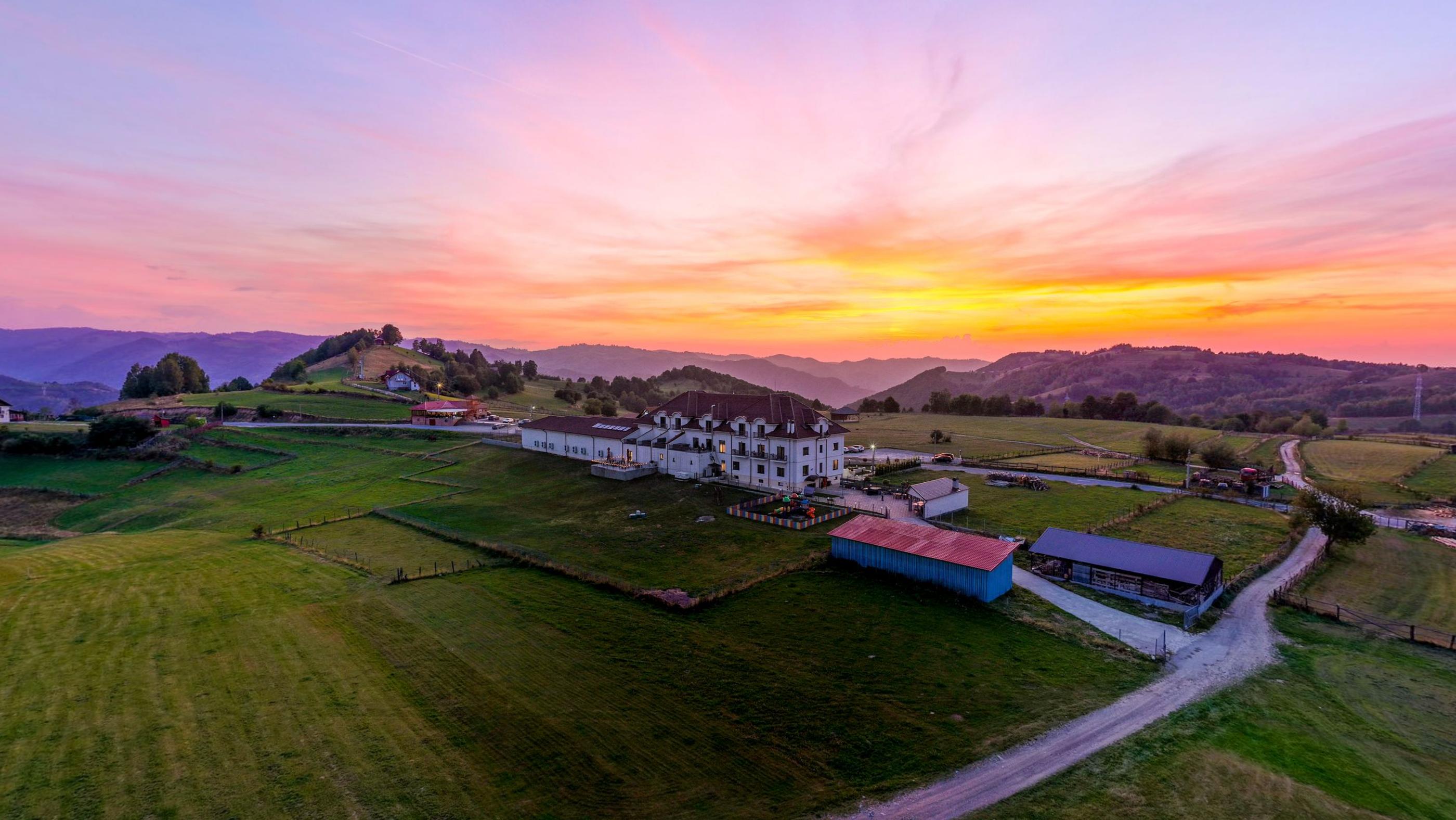 Magura Jina hotel on a green ridge above Jina at sunset, with the Cindrel mountains behind