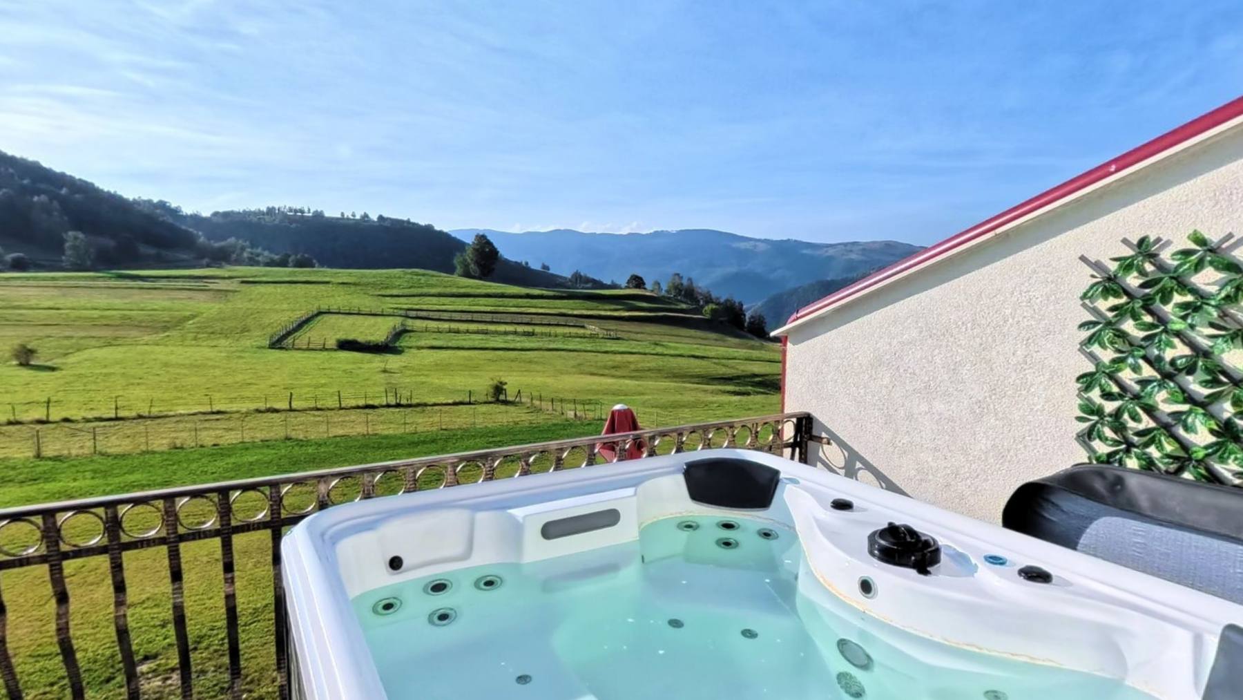 An outdoor jacuzzi on a terrace looking across green pasture to the mountains