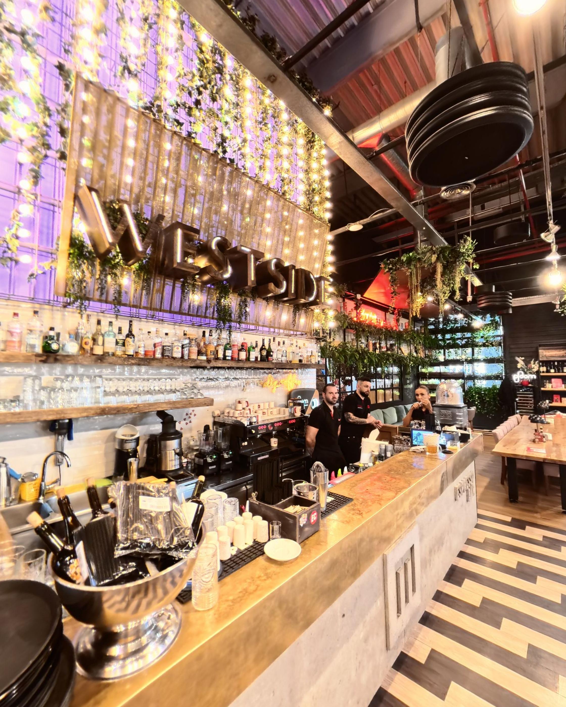 The lit bar with bottles, greenery and staff working behind it