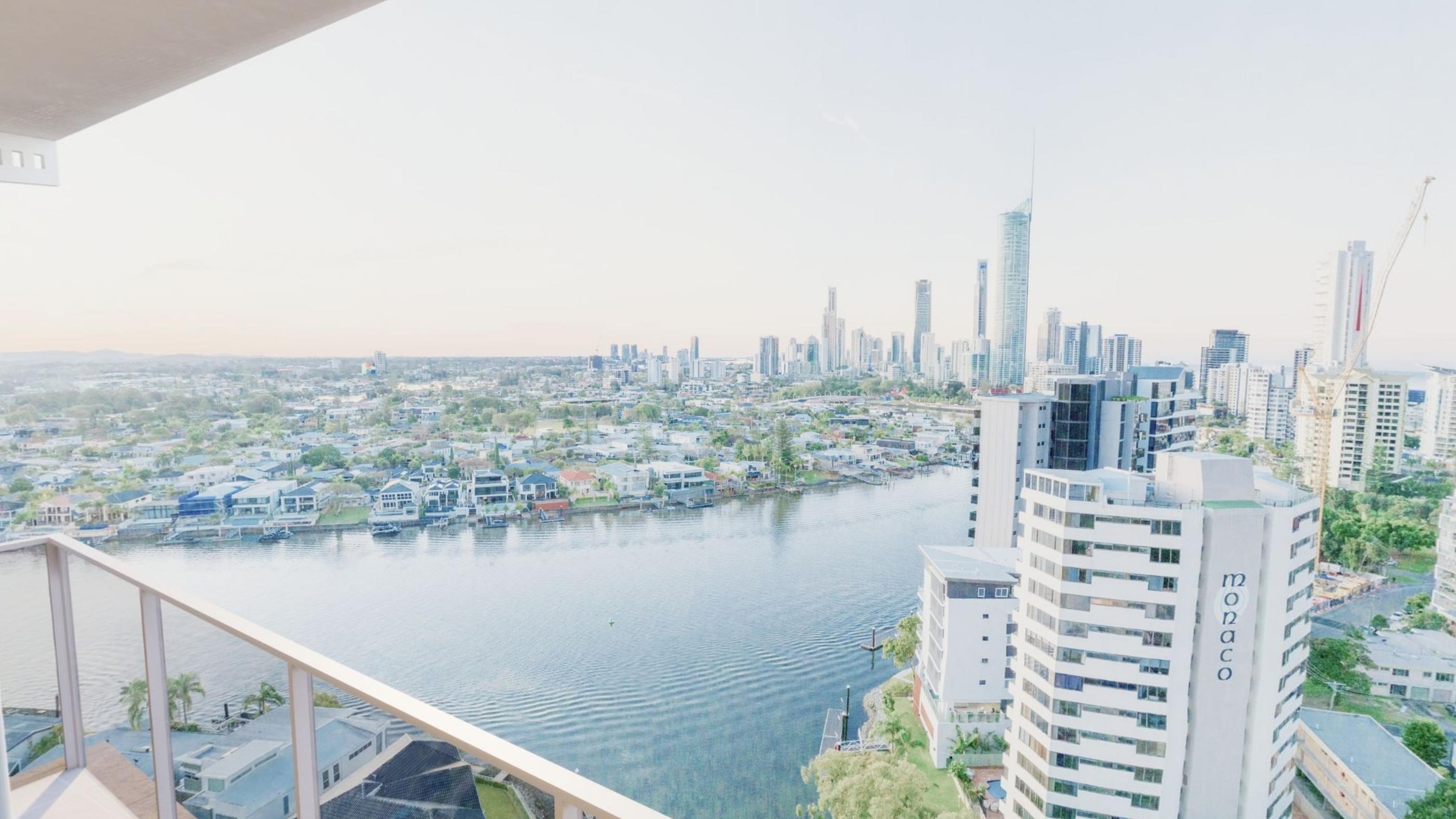 A wide terrace view over a river and low rooftops toward distant city towers