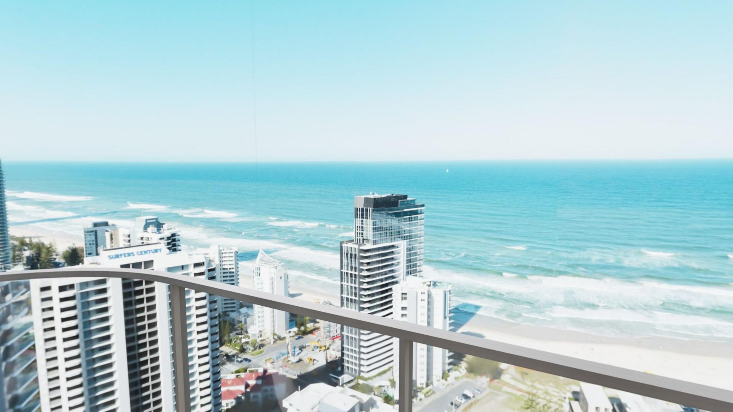 A balcony rail high above a long beach with surf and towers along the shoreline