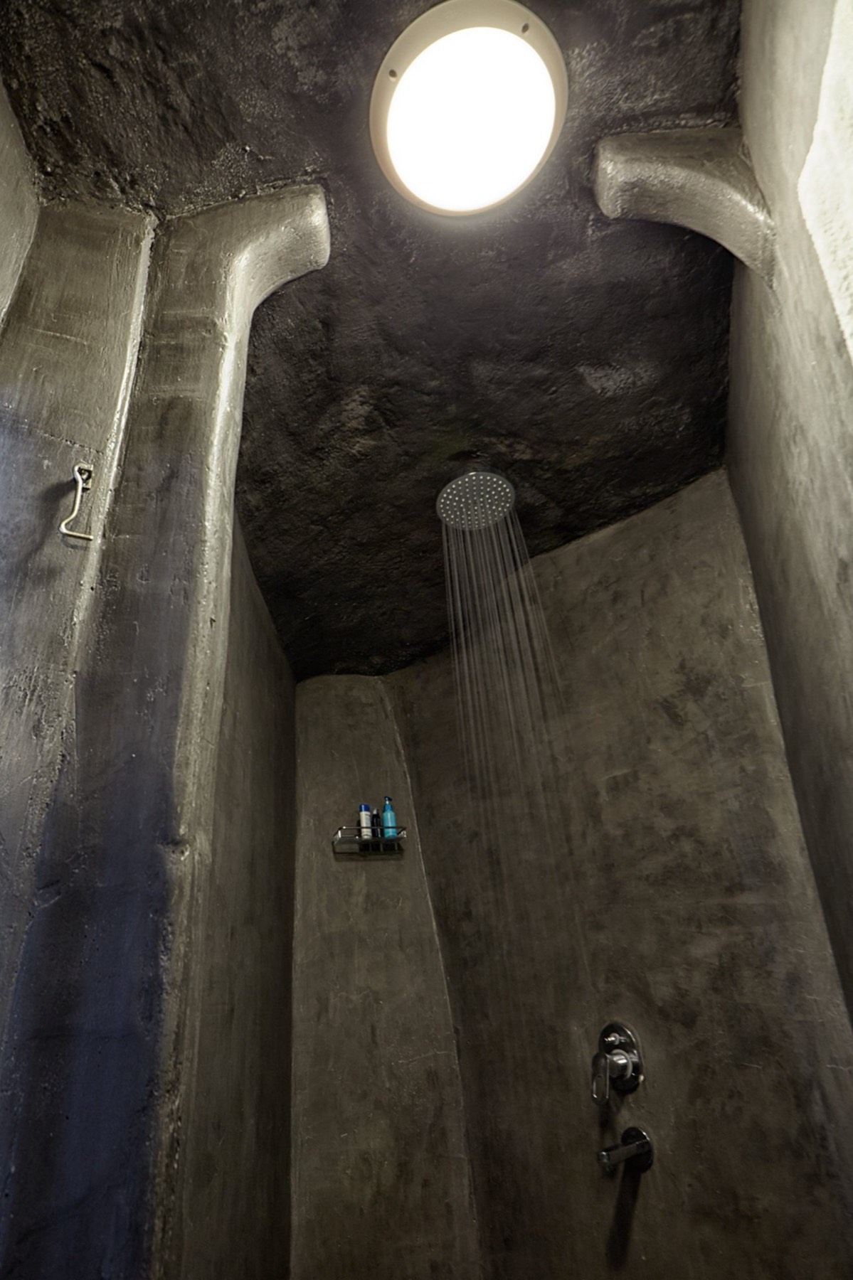 A rain shower under a round skylight in a bathroom carved from volcanic rock