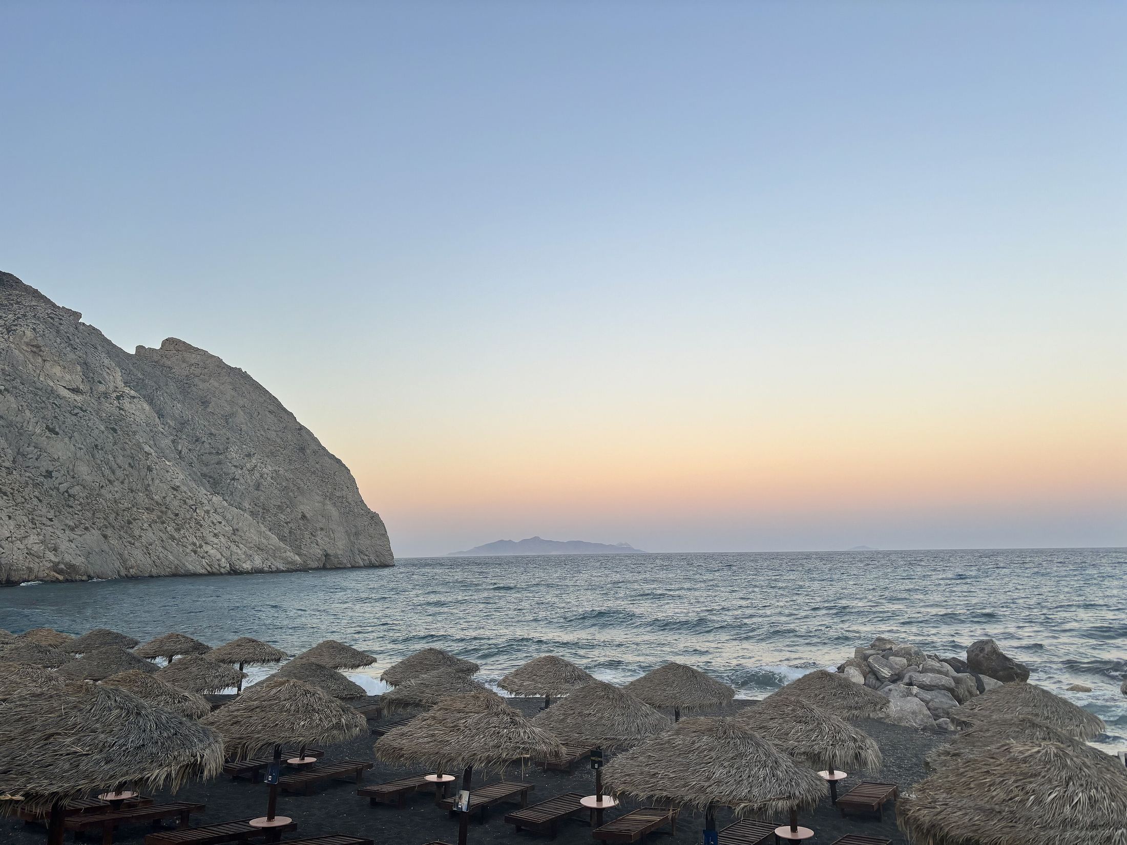 Perissa beach at sunset below the Mesa Vouno headland, with straw parasols on black sand