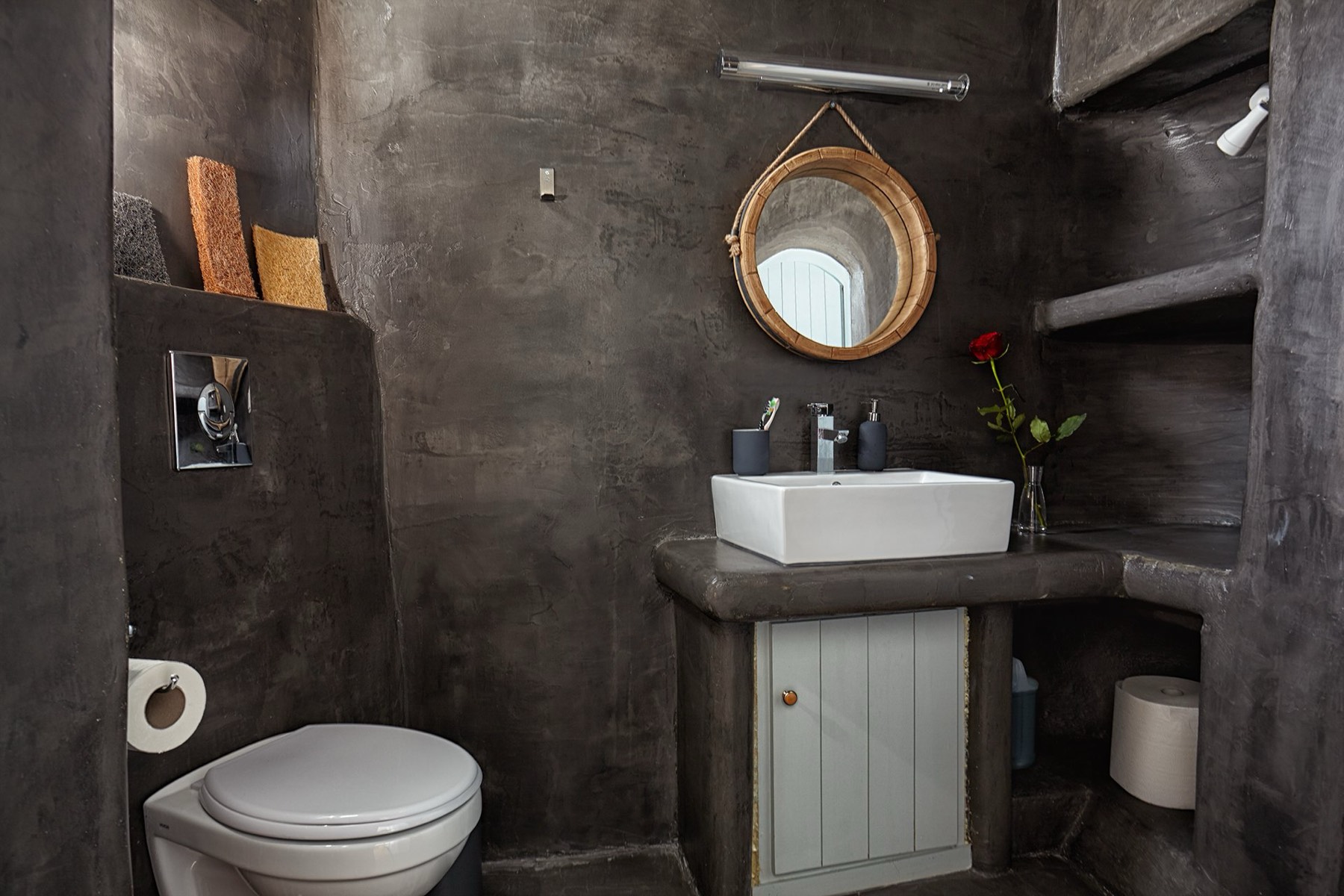 Polished dark stone washbasin and round rope mirror in the cave bathroom