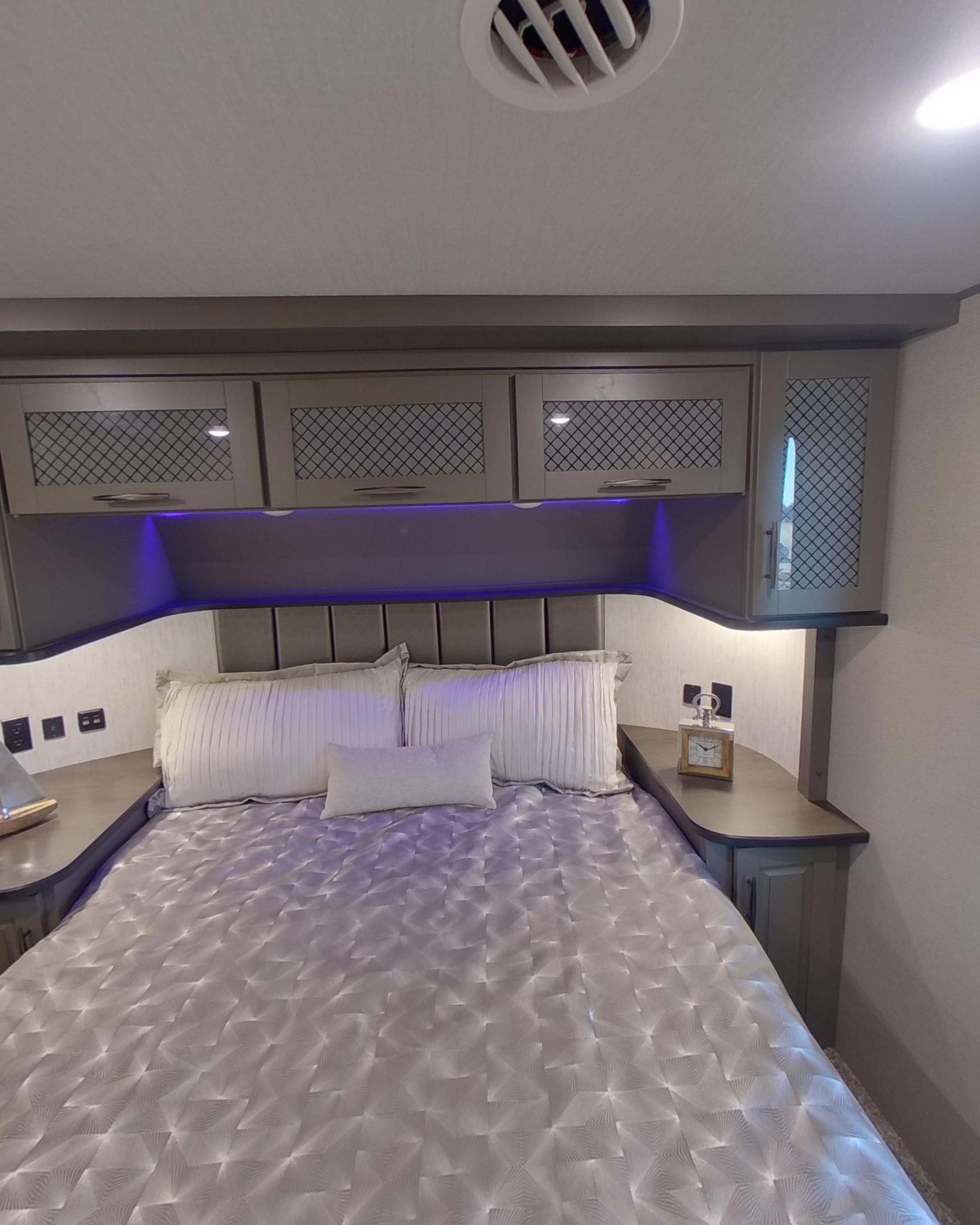 The bedroom with a made bed under overhead lockers and violet cove lighting