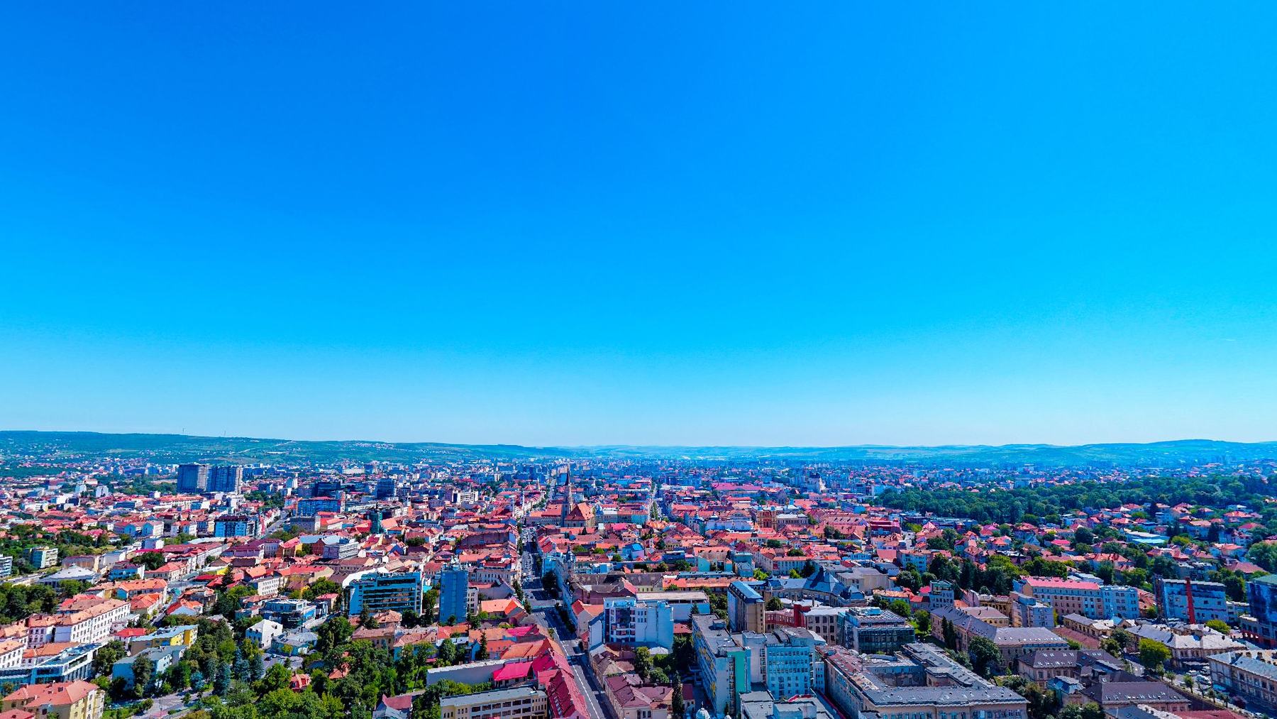 Cluj-Napoca seen from above on a clear afternoon, rooftops running to the hills