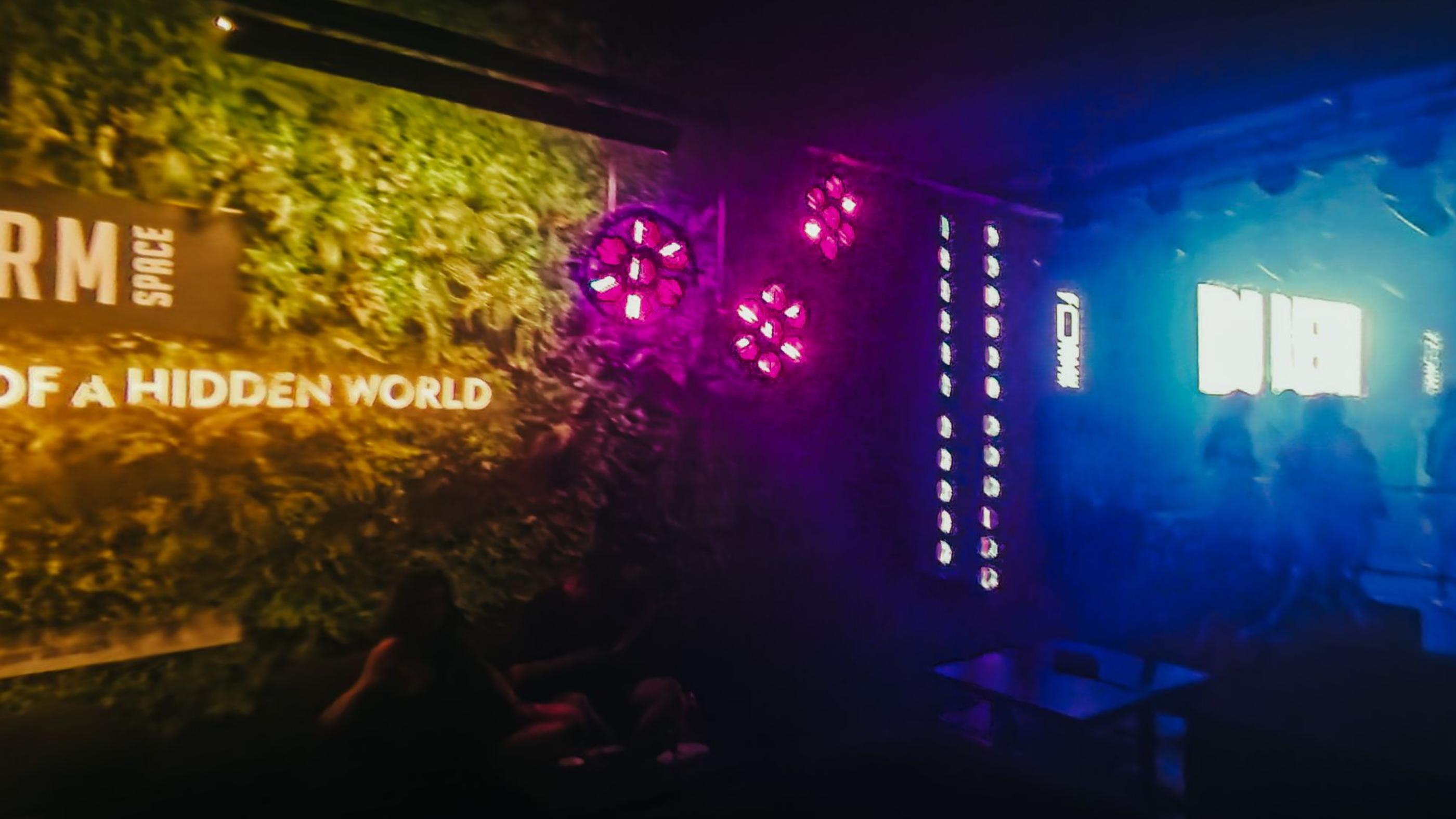 A darkened space lit in pink and blue, with a sign reading unlock the magic of a hidden world