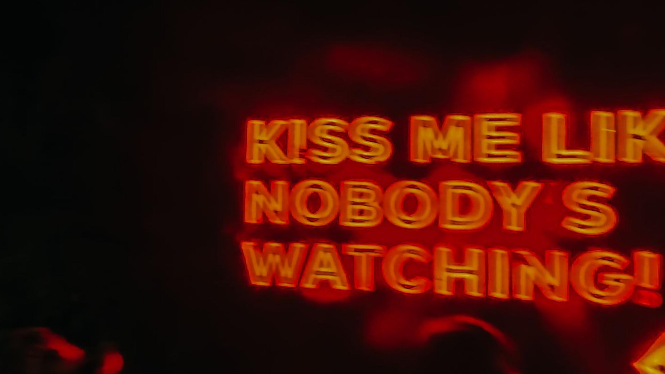 A neon sign reading kiss me like nobody is watching